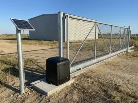 Chain-link slide gate at an equipment yard, with a gate opener and a solar panel on a post