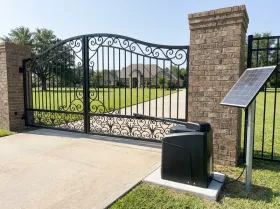Driveway gate of a home on a wide lawn, with a gate opener and a solar panel on a post