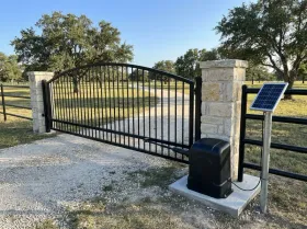 Ranch entrance gate on a long gravel driveway, with a gate opener and a solar panel on a post