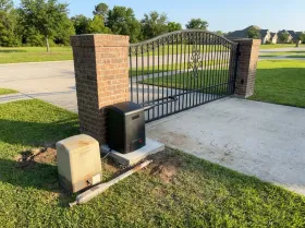 New black gate opener at a driveway gate, with the old opener removed and set on the grass