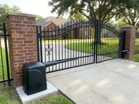 Wrought-iron swing gate across a home driveway with a gate opener beside it