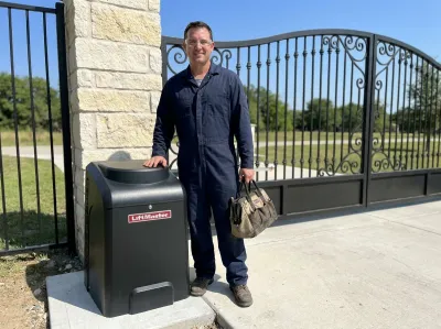 Gate mechanic with a tool bag standing beside a black LiftMaster gate opener