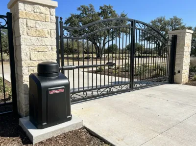 Black LiftMaster swing gate opener on a concrete pad beside an ornamental iron gate