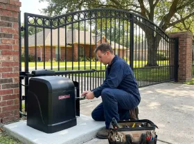 Mechanic working at a gate opener beside a home driveway gate